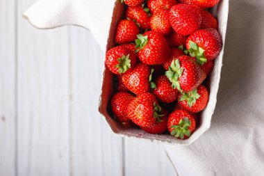 Kağıt sepette taze çilek. Beyaz masa örtüsü üzerinde tatlı kırmızı böğürtlen. Sağlıklı ve organik tatlı..
