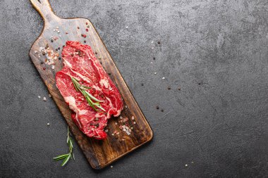 Tahta kesme tahtasında çiğ et. Büyük bir parça pişmemiş kırmızı et ve arka planda biberiye ve fotokopi alanı var..