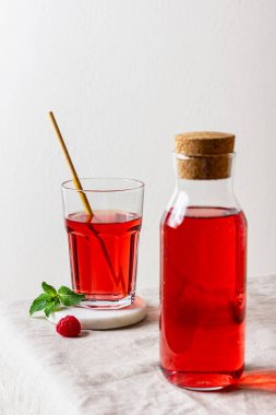 Bardakta ahududu içeceği, arka planda da şişe. Böğürtlen limonatası. Yan görünüm.