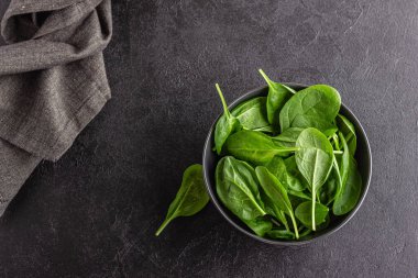Taze yeşil ıspanak yaprakları kasede. Siyah masada doğal vejetaryen yemekleri..