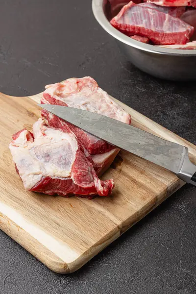 Büyük bir bıçakla ahşap kesme tahtasında pişmemiş taze sığır pirzolası. Koyu arkaplanda çiğ kırmızı et parçaları.