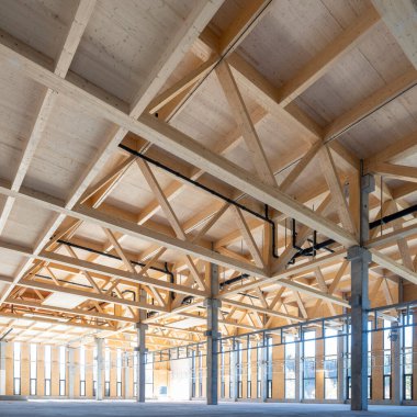 Kereste kirişleri ve birçok cam cephe elementi olan prefabrik beton sütunlarla modern endüstriyel salon.