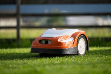 Robotik çim biçme makinesi yeni kesilmiş yeşil yemyeşil çimlerle çevrili bir bahçede çalışıyor.