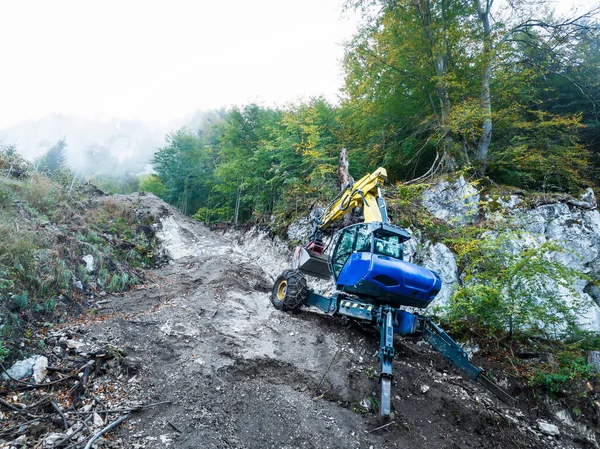 ケーブルのトレンチを掘っている間 山林の非常に急な 困難な岩の地形の掘削機またはホッピング掘削機 ストック写真