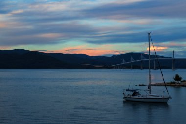 Beautiful modern bridge over the sea on Peljesac in Croatia. In the foreground houses and in the background the Peljesac mountains. Dramatic sky with clouds.