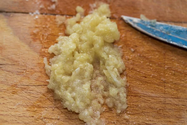 Crushed garlic cloves are salted on a wooden cutting board.
