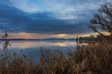 Akşamın erken saatlerinde gölet çevresindeki kış manzarası. Gökyüzünde dramatik bulutlar.