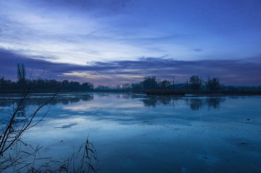 Donmuş bir göletin kış manzarası. Gün batımından bir saat sonra. Güzel bulutlar ve donmuş gölet yüzeyi.