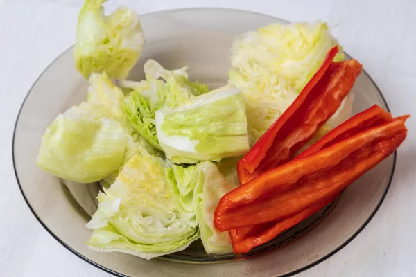 Healthy food. Iceberg salad and red pepper on a plate. The background is white.