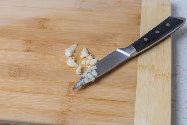 A crushed clove of garlic on a wooden cutting board. The knife lies next to the garlic.