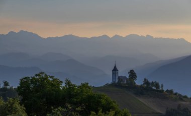 Slovenya 'nın Jamnik köyündeki Aziz Primoz Kilisesi, Avrupa. Kilise dağların yamacında. Gündoğumu, arka planda dağ zirveleri.