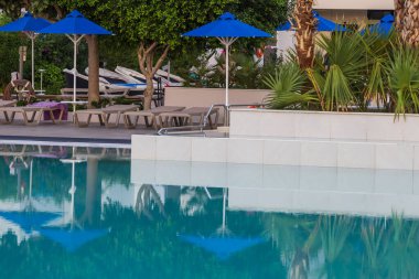 Deniz Burnu. Havuzun kenarındaki sandalyeler ve şemsiyeler suya yansıyor..