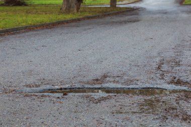 Asfalt yol ıslak ve çukurlar suyla dolu..