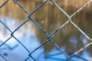 Tel örgülerin örgüsü. Çitin arkasında bir gölet var..