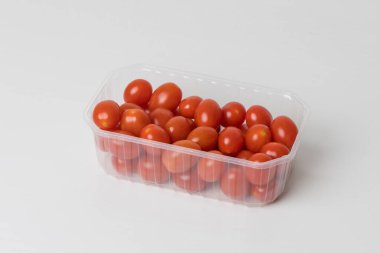Beyaz arka planda plastik kasede küçük kırmızı kiraz domatesleri.