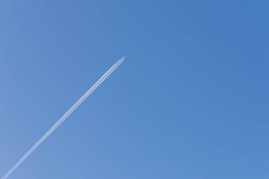 Bulutsuz mavi gökyüzünde bir uçak. Uçağın arkasında bir uçuş yolu var.