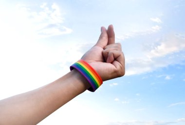 El ve bilekliklerde gökkuşağı bileklikleri, bulanık mavi arka plan, lgbtq + cinsiyet kutlamaları, cinsiyet özgüveni konsepti ve tüm insanları gurur ayında insan haklarına saygı duymaya çağırma.