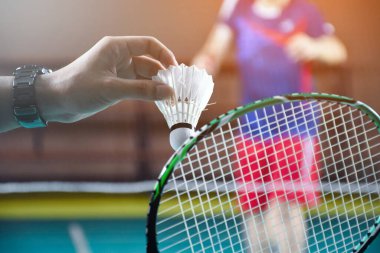 Badminton oyuncusu, raketi ve beyaz kremalı mekikçiyi sahanın diğer tarafına götürmeden önce kalenin önünde tutuyor..