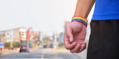 Gökkuşağı bileklikleri ve gökkuşağı bayrakları el ele tutuşuyor, tüm dünyada gurur ayında lgbtq + cinsiyetlerinin kutlanması konsepti, yumuşak ve seçici odaklanma.