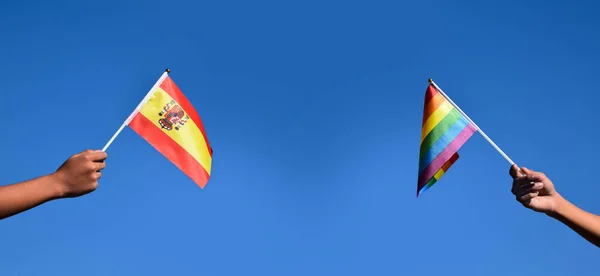 西班牙国旗和彩虹旗手挽手 反对蓝调背景 软而有选择的焦点 世界各国骄傲月的性别庆祝理念 — 图库照片