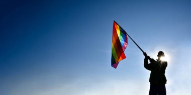 Gökkuşağı bayrağı mavi arka planda el ele tutuşuyor, LGBT konsepti gururlu bir ayda, Haziran ayında, tüm dünyada.