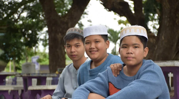 学校の公園に座って読書をしたり 勉強をしたり 宿題を相談したり 学校で宗教的な科目を学ぶのを待っている若いアジアのイスラム教徒やイスラム教徒の男の子 柔らかく選択的な焦点 — ストック写真