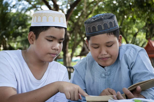 Asian muslim boys sit together in school park to read and learn their daily activity and do homework in their free times before going back home, soft and selective focus.