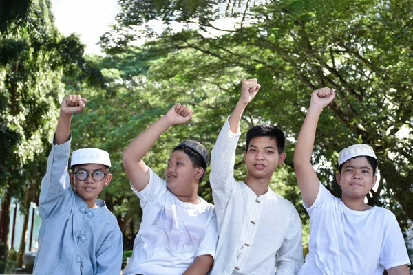 年轻的亚洲穆斯林男孩们举起他们的右手 在学校公园的一棵树下快乐地展示他们的胜利和成功 他们的注意力是柔软而有选择的 — 图库照片