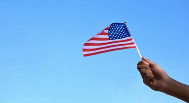 Amerikan ulusal bayrağı elinde ve mavi gökyüzü arka planında dalgalanıyor, yumuşak ve seçici odaklı..
