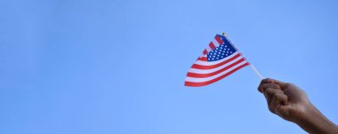 Amerikan ulusal bayrağı elinde ve mavi gökyüzü arka planında dalgalanıyor, yumuşak ve seçici odaklı..