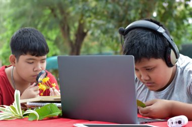 Ödev yapan, bilgi arayan ve çeşitli tropikal orman türleri hakkındaki haberleri dizüstü bilgisayarlar, büyüteçler, not defterleri, cep dürbünleri ve tabletler kullanarak yapan Asyalı genç çocuklar, yumuşak odaklanma.