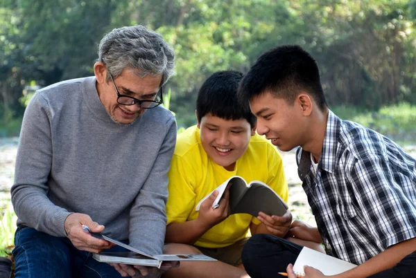 一位年事已高的亚裔男子正把业余时间花在解释课程内容上 并高兴地帮助他的两个孙子在他的后院做家庭作业和做学校的项目 心情舒畅 — 图库照片