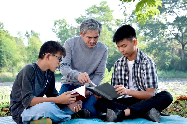 一位年事已高的亚裔男子正把业余时间花在解释课程内容上 并高兴地帮助他的两个孙子在他的后院做家庭作业和做学校的项目 心情舒畅 — 图库照片