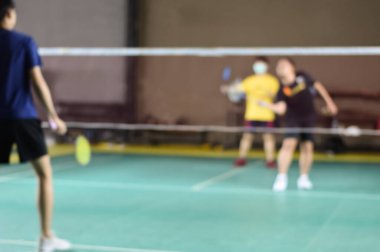 Blurred image of badminton player holds racket and white cream shuttlecock in front of the net before serving it to another side of the court.