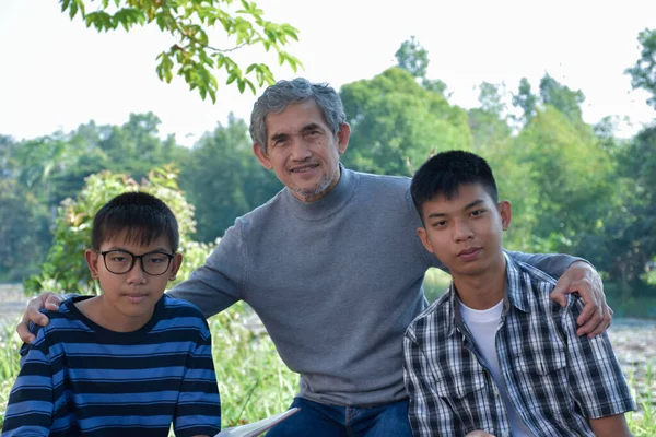 Asian elder and grandsons are spending time together in the park by teaching, reading and talking about topic in the book which they are interested in happily, soft  and selective focus on first boy.