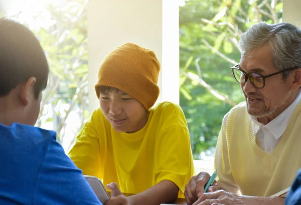 Asian elderly male teacher is helping students to do the school project work by teaching the correct order and process of doing research projects and Internet reference resources.