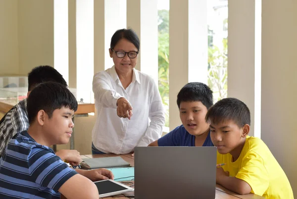 asian boys and asian elderly female teacher who are inside the room, they are doing school project work and listening to their elderly teacher about their project work.