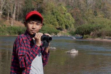 Asian boys are using binoculars to do the birds' watching in tropical forest during summer camp, idea for learning creatures and wildlife animals and insects outside the classroom.