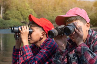 Asian boys are using binoculars to do the birdwatching in tropical forest during summer camp, idea for learning creatures and wildlife animals and insects outside the classroom.
