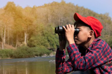 Asian boys are using binoculars to do the birds' watching in tropical forest during summer camp, idea for learning creatures and wildlife animals and insects outside the classroom.