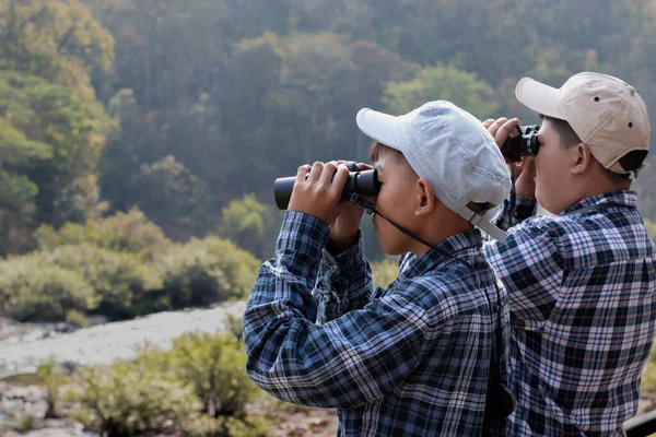 Asian boys are using binoculars to do the birdwatching in tropical forest during summer camp, idea for learning creatures and wildlife animals and insects outside the classroom.