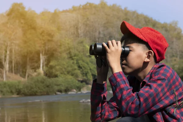 Asian boys are using binoculars to do the birds' watching in tropical forest during summer camp, idea for learning creatures and wildlife animals and insects outside the classroom.