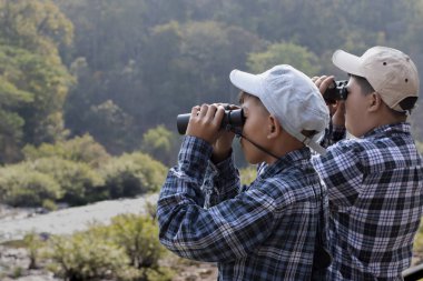 Asian boys are using binoculars to do the birdwatching in national park during their summer vacation, idea for learning creatures, wildlife animals, insects, trekking and hiking outside the classroom.