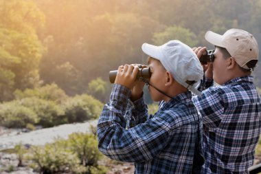 Asian boys are using binoculars to do the birdwatching in national park during their summer vacation, idea for learning creatures, wildlife animals, insects, trekking and hiking outside the classroom.