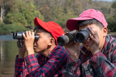 Asian boys are using binoculars to do the birdwatching in national park during their summer vacation, idea for learning creatures, wildlife animals, insects, trekking and hiking outside the classroom.