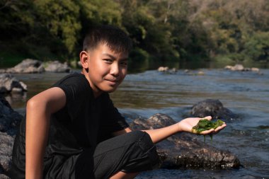 Asian schoolboy holding freshwater algae from diving into the river and pulling it up to study the fertility of the river's nature and including to do freshwater algae in his environment project work.