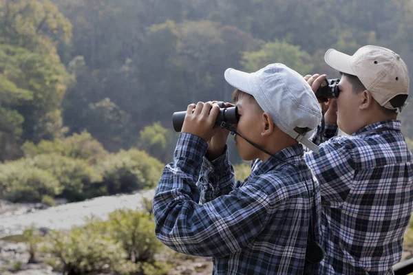 Asian boys are using binoculars to do the birdwatching in national park during their summer vacation, idea for learning creatures, wildlife animals, insects, trekking and hiking outside the classroom.