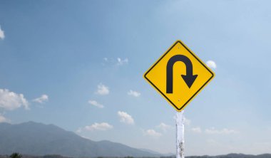 Trafik işareti: Kırsal yolun yanındaki çimento direğinde sağa U dönüşü işareti, beyaz bulutlu mavi arka plan, boşluğu kopyala.