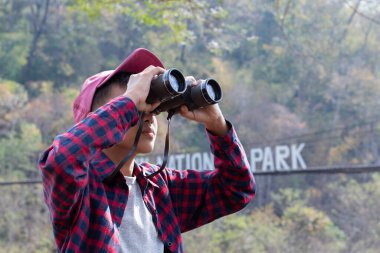 Asian boy held binoculars in hands and doing the bird watching, fish watching and forest observing in local national park, asian children summer vacation concept.