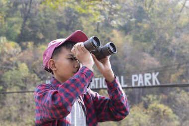 Asian boy held binoculars in hands and doing the bird watching, fish watching and forest observing in local national park, asian children summer vacation concept.
